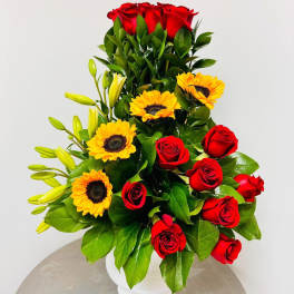 Red roses and yellow sunflowers arranged in a white vase