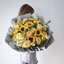 Bouquet of yellow sunflowers and cream roses wrapped in gray paper