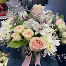 Pink roses and white flowers arranged in a glass vase with a pink ribbon