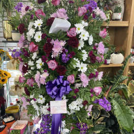 Large standing spray of pink, white, and purple flowers with a purple ribbon
