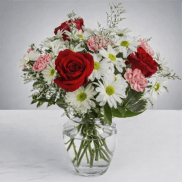 Bouquet of red roses, white daisies, and pink carnations in a clear glass vase