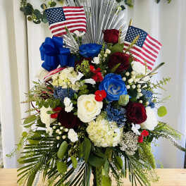 Large patriotic floral arrangement with red, white, and blue roses and flags