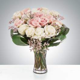 Pink and white roses in a clear glass vase with broad green leaves