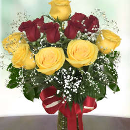 Bouquet of yellow and red roses in a glass vase with a red ribbon