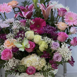 Mixed bouquet in a white wicker basket with pink, purple, and cream flowers