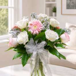 Bouquet of white roses and pink gerbera daisies in a glass vase with a silver bow.