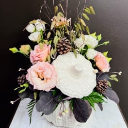 Pink and white flowers arranged in a white pumpkin-shaped vase with pinecones