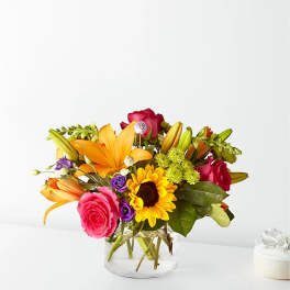 Mixed bouquet of roses, lilies, and a sunflower in a glass vase