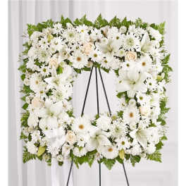 White floral wreath on a black easel with lilies and daisies