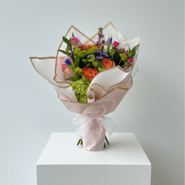 Bouquet of orange, pink, and purple flowers wrapped in pale pink paper