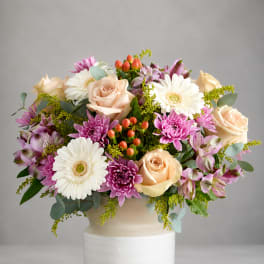 Mixed bouquet of roses, gerbera daisies, and purple blooms in a white vase