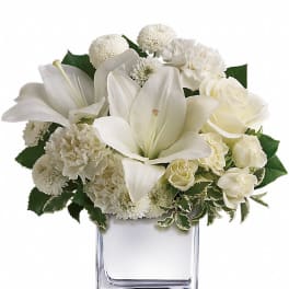White lilies, roses, carnations, and mums arranged in a clear square glass vase