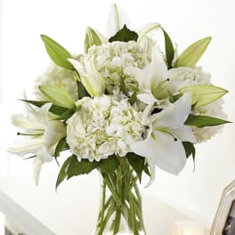 White lilies and hydrangeas arranged in a clear glass vase
