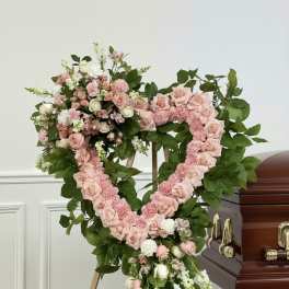 Heart-shaped pink floral funeral wreath on a stand beside a casket