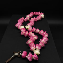 Pink and white rose petals arranged in a rosary shape with a crucifix