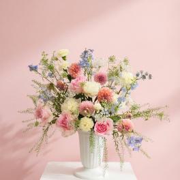 Pastel mixed flower arrangement in a white vase on a pedestal