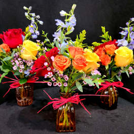 Three mixed rose bouquets in amber glass vases with pink ribbon ties