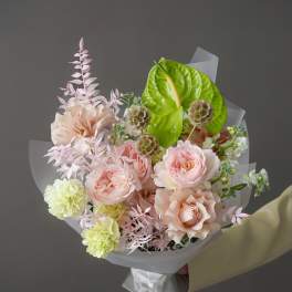 Bouquet of blush roses, pale carnations, and green anthurium in clear wrap