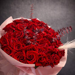 Large bouquet of tightly clustered red roses wrapped in pale paper with dark accents