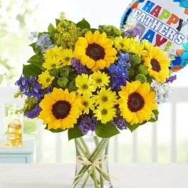 Bouquet of sunflowers, yellow daisies, and purple flowers in a glass vase