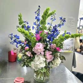 Tall mixed bouquet in a clear glass vase with pink, white, blue, and green flowers.
