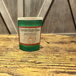 Green jar candle with an apple cinnamon label on a wooden surface