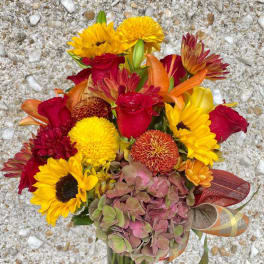 Bouquet of red roses, yellow sunflowers, and orange blooms in a glass vase