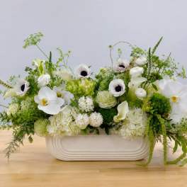 White floral arrangement in a low rectangular vase with green accents
