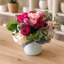 Pink and peach rose bouquet in a white vase with a striped ribbon