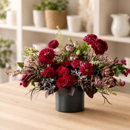 Red and pink floral arrangement in a black vase on a table