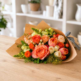 Bouquet of orange and peach roses with mixed blooms wrapped in brown paper