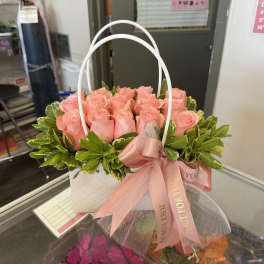 Pink roses arranged in a white handled gift basket with a pink ribbon