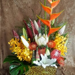 Tropical floral arrangement with orange heliconia and white lilies in a decorative container