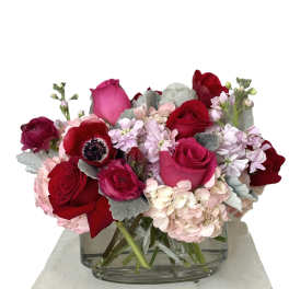 Red and pink roses with pale hydrangeas in a clear glass vase