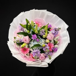 Round bouquet of pink, purple, and white flowers wrapped in white paper