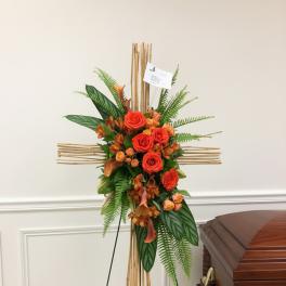 Orange rose funeral spray on a bamboo cross stand beside a casket
