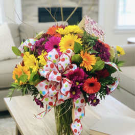 Colorful mixed flower bouquet in a glass vase with a polka-dot ribbon