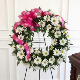 White daisy wreath with a bright pink ribbon on a black stand