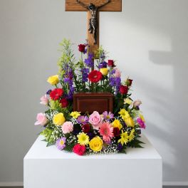 Colorful funeral floral arrangement beneath a wooden crucifix