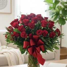 Red roses arranged in a clear glass vase with a red ribbon bow