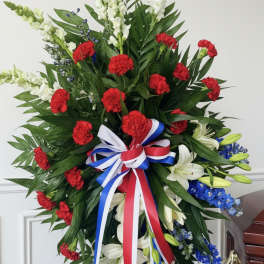 Large standing floral spray with red carnations, white lilies, and blue flowers