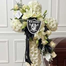White floral standing spray with lilies and a Raiders emblem