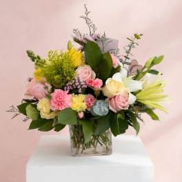 Mixed bouquet of pink, yellow, and white flowers in a clear square vase