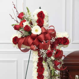 Cross-shaped floral tribute with red roses, white flowers, and a large red ribbon