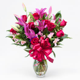 Bouquet of pink lilies and red roses in a clear glass vase with a pink ribbon