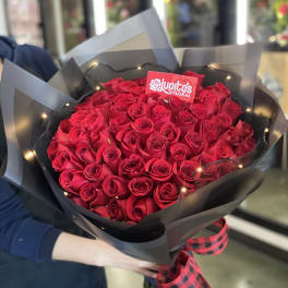 Large bouquet of red roses wrapped in black paper with a plaid ribbon
