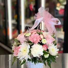Pink and white flowers arranged in a white basket with a pink ribbon
