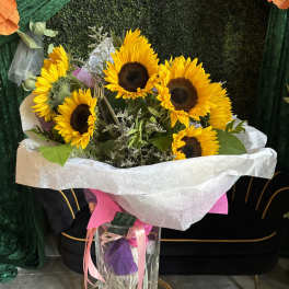 Bouquet of sunflowers in a clear glass vase with pink ribbon