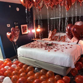 Bedroom decorated with heart balloons and rose petals on the bed