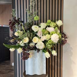 Large floral arrangement in a white pedestal vase with white, pale pink, and green blooms
